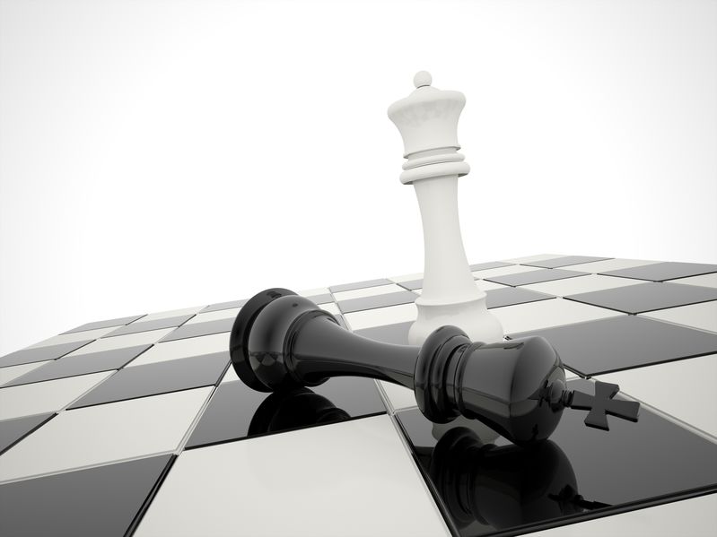 White chess queen standing over a toppled black king on a chessboard